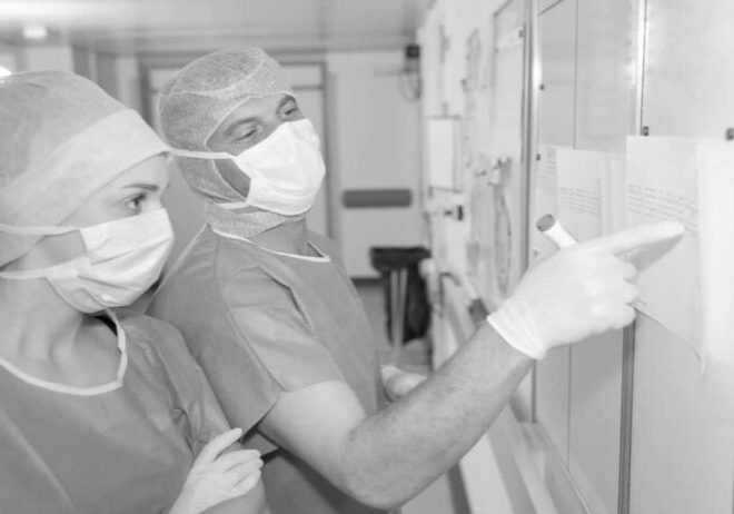 Doctor and nurse in PPE planning patient schedules on whiteboard in procedure area